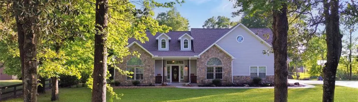 A large, inviting home nestled in a wooded area, with a prominent driveway that enhances its charming appeal.