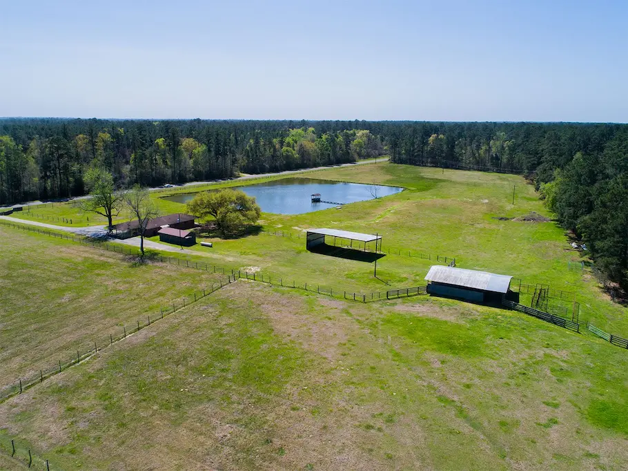 Aerial view of a picturesque farm featuring a serene pond and a rustic barn, showcasing the property's expansive landscape.