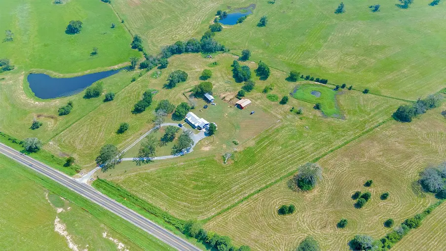 Aerial view showcasing a picturesque farm bordered by a winding road, highlighting the property's expansive landscape.
