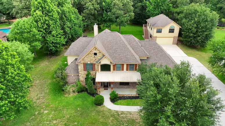 Aerial view of a home featuring a spacious driveway and surrounding trees