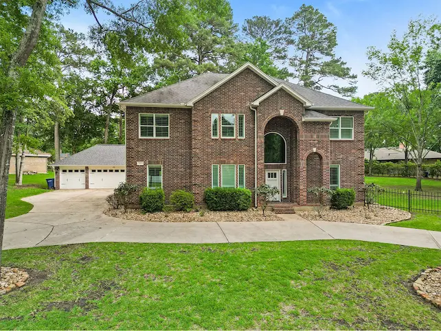 Charming brick home featuring a spacious driveway and lush trees