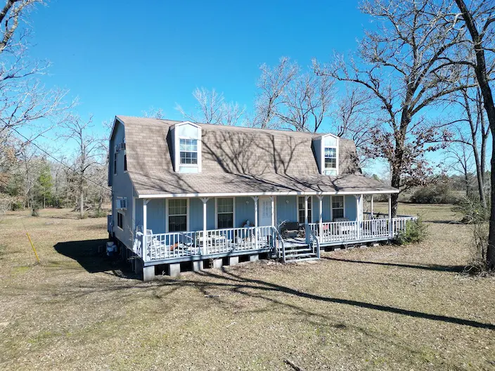 A charming blue house with a welcoming porch, surrounded by lush green trees, perfect for a cozy family home.