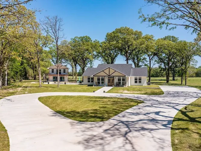 Charming home featuring a spacious driveway and lush trees, perfect for a serene living experience.