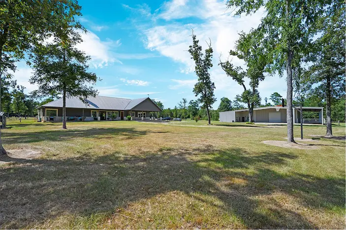 Expansive grassy space surrounded by trees, featuring a well-maintained house in the background