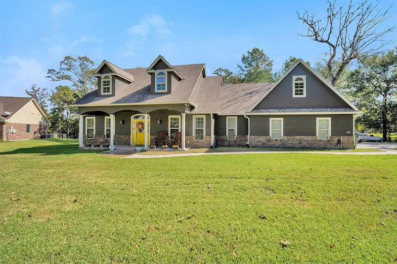 A charming gray house featuring a bright yellow door, surrounded by a lush green lawn