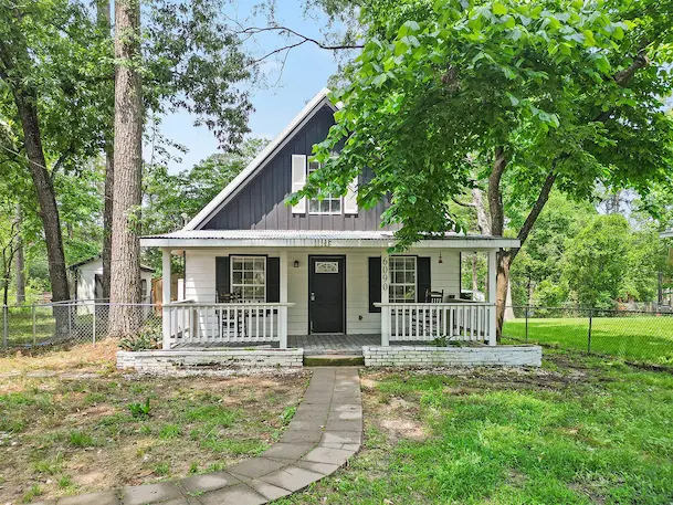 A charming small house with a welcoming porch and a lush tree in the front yard