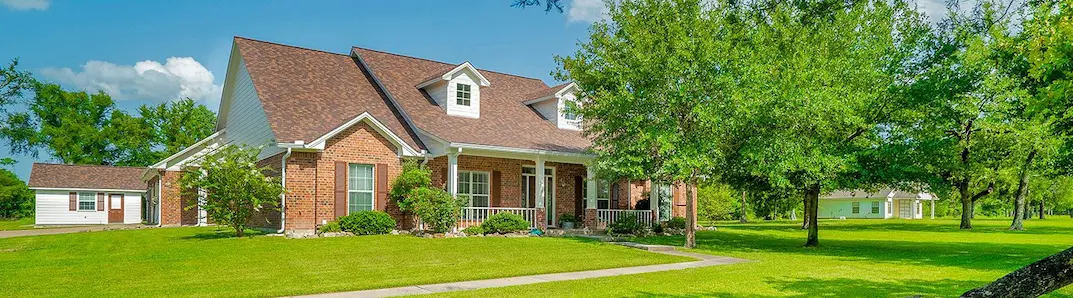 A spacious brick house surrounded by a well-maintained lawn and mature trees, ideal for family living and outdoor activities.
