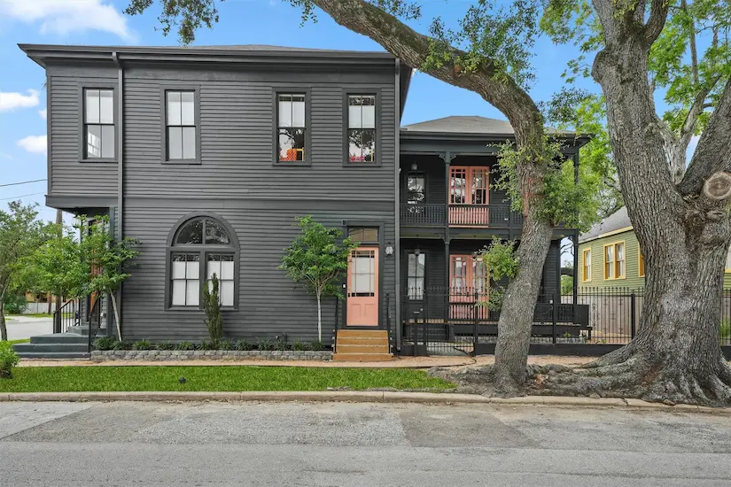 Two-story house with black siding, surrounded by a lush tree, showcasing modern architecture and inviting curb appeal.