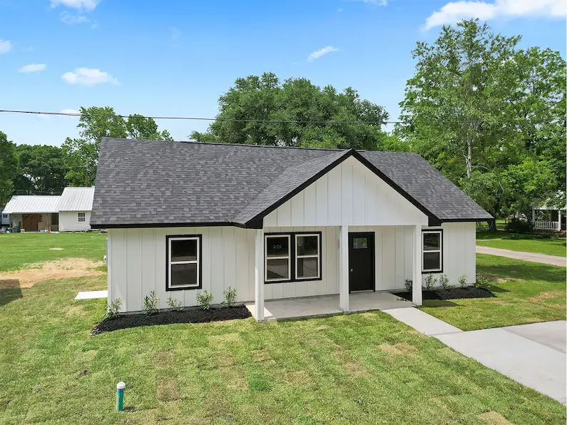 A small white house featuring a black roof, showcasing a charming and classic architectural style.