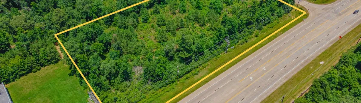 Aerial view of a vacant wooded lot, marked with a yellow line, showcasing potential for development or investment.