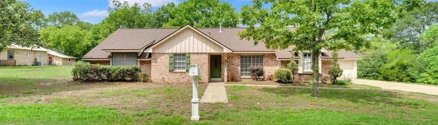 Charming brick home featuring a spacious driveway and mature trees, perfect for a welcoming family atmosphere.