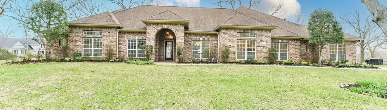 a brick home surrounded by a large yard and trees, highlighting the property's outdoor space.