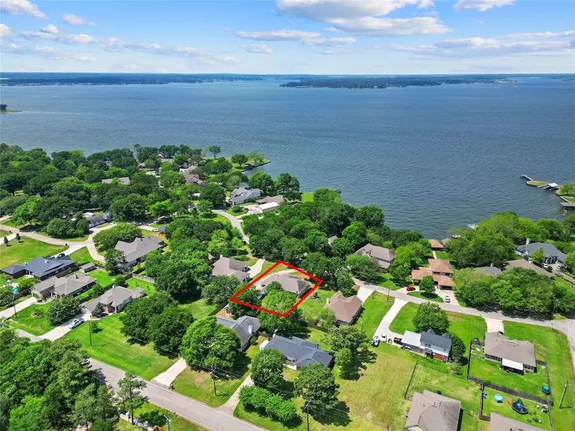 Aerial view of a home surrounded by a lake and trees, highlighting a selected lot with a red outline.
