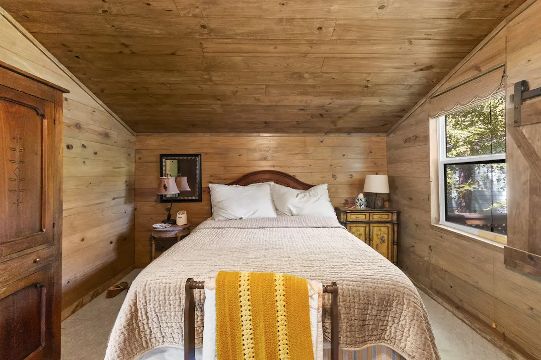 A cozy bedroom featuring a neatly made bed beneath a warm wooden ceiling