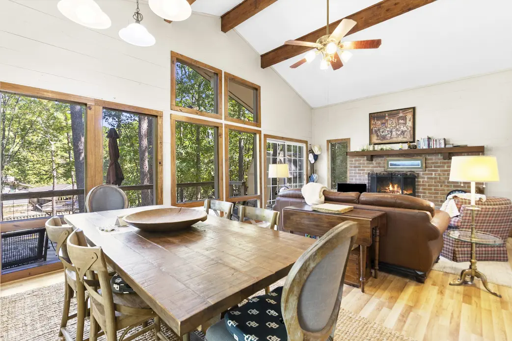 a cozy living room featuring a table, chairs, a fireplace, and a large window letting in natural light.