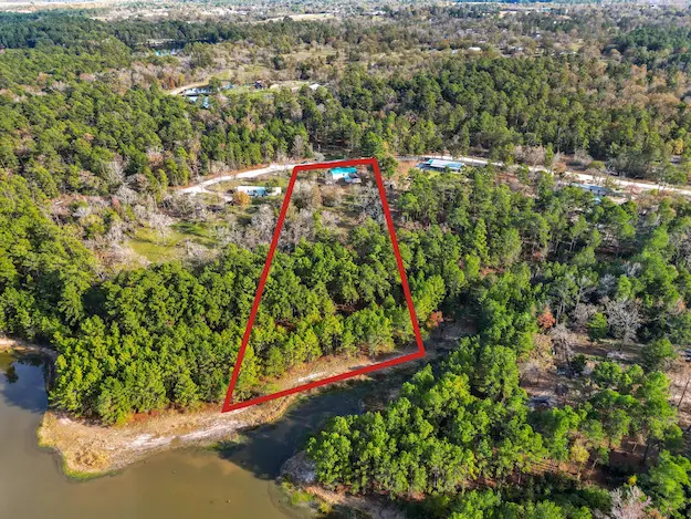 Land for sale in a wooded area near a serene lake, highlighted by a red line marking the selected lot boundaries.