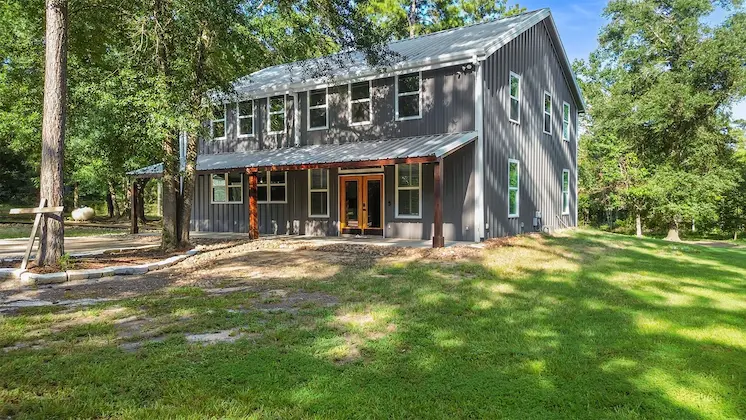 A charming gray house featuring a covered porch, surrounded by lush trees